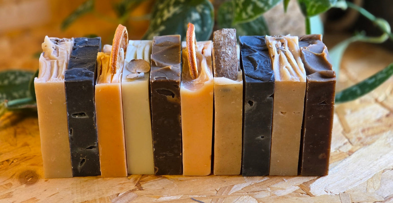 Row of handmade soap bars with natural textures on a wooden surface with plants in the background