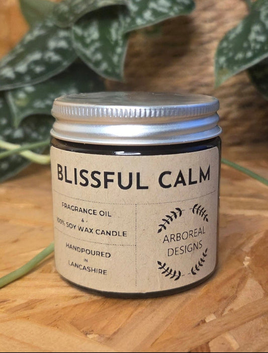 Candle labeled 'Blissful Calm' on a wooden surface with plants in the background